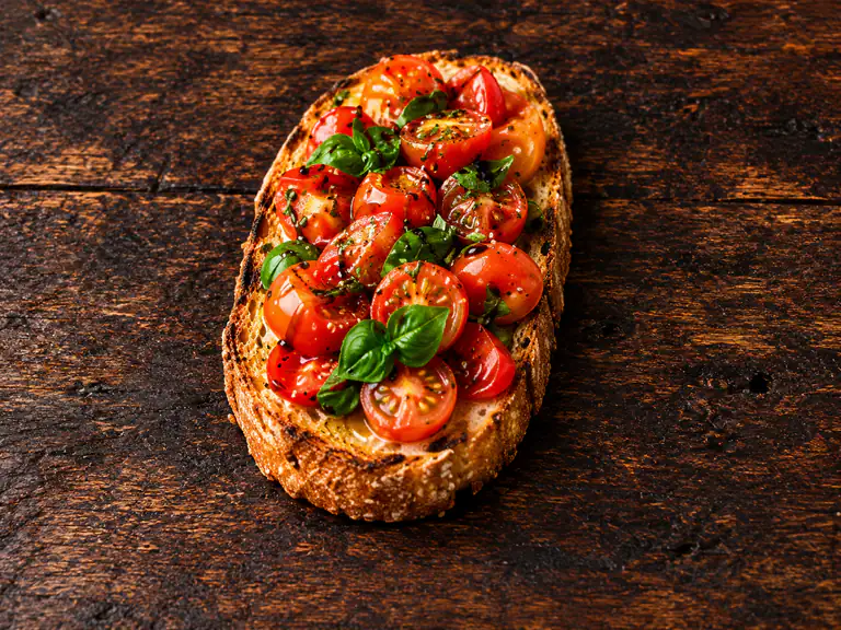 Bruschette al pomodoro con la farcitura su pane casereccio tostato, fotografate su un piano di legno scuro