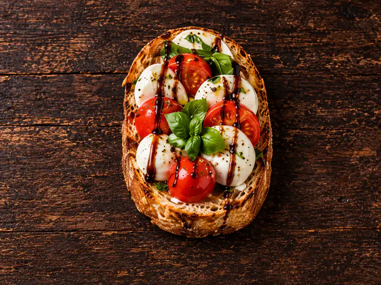 Bruschette caprese con la farcitura su pane casereccio tostato, fotografate su un piano di legno scuro