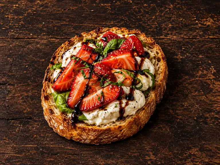 Bruschette con burrata e fragole con la farcitura su pane casereccio tostato, fotografate su un piano di legno scuro