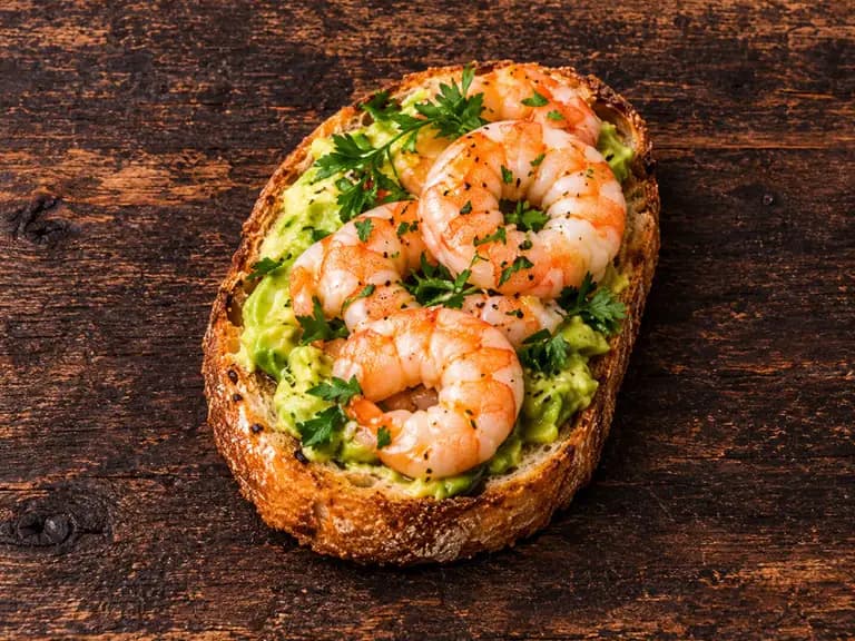 Bruschette con gamberi e avocado con la farcitura su pane casereccio tostato, fotografate su un piano di legno scuro