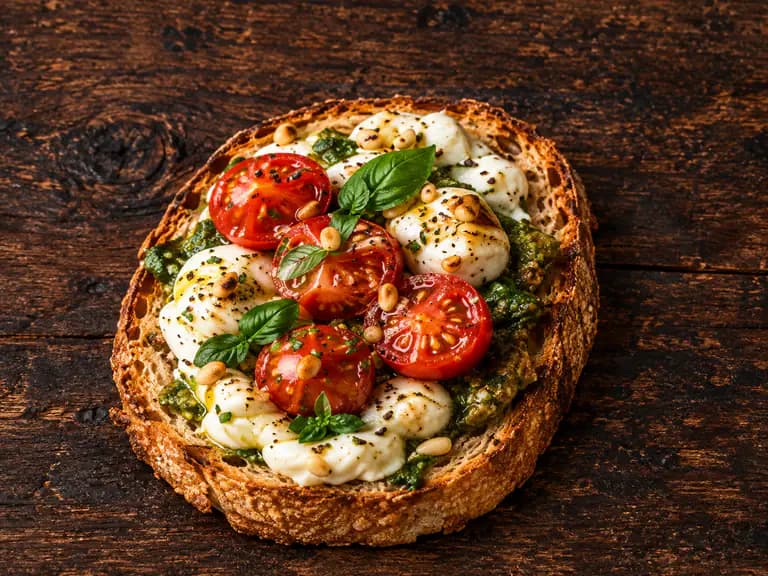 Bruschette con mozzarella e pesto con la farcitura su pane casereccio tostato, fotografate su un piano di legno scuro