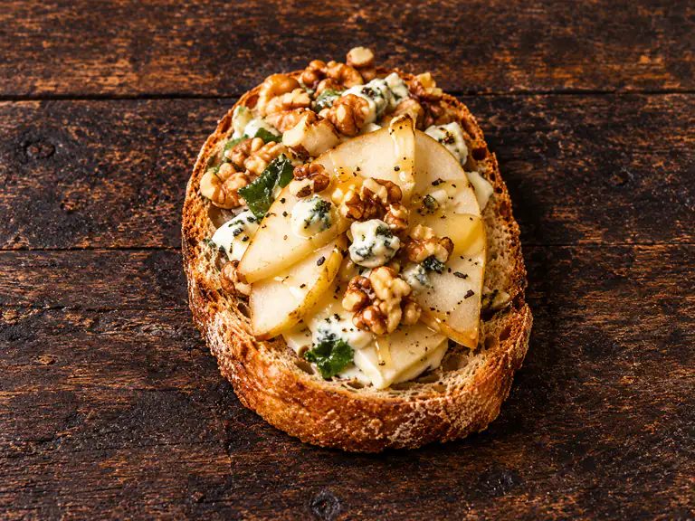 Bruschette con pere e gorgonzola con la farcitura su pane casereccio tostato, fotografate su un piano di legno scuro