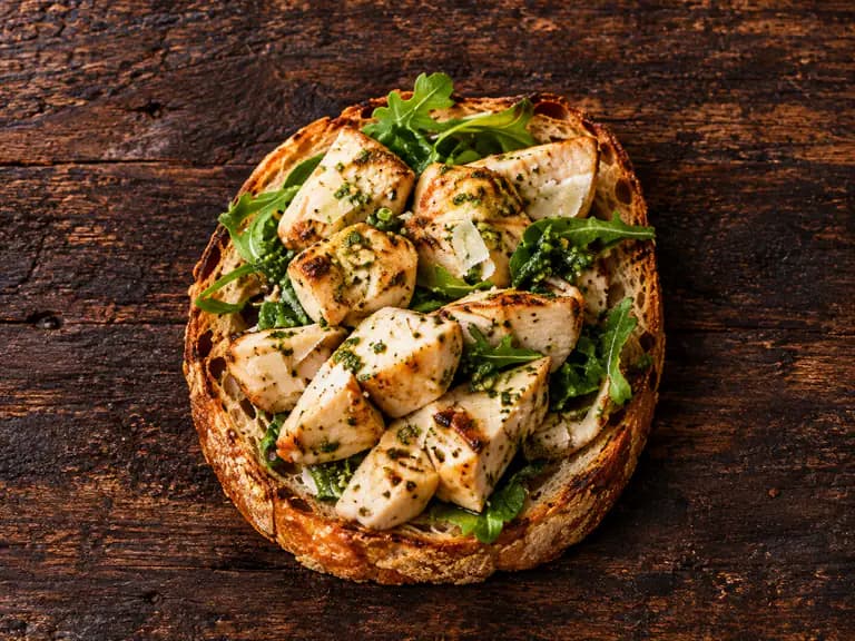 Bruschette con pollo e pesto con la farcitura su pane casereccio tostato, fotografate su un piano di legno scuro