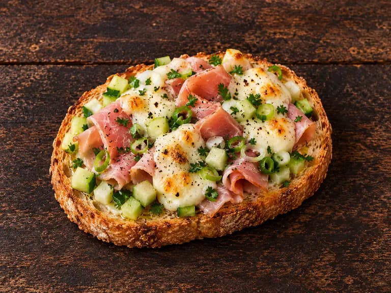 Bruschette con prosciutto cotto e formaggio con la farcitura su pane casereccio tostato, fotografate su un piano di legno scuro