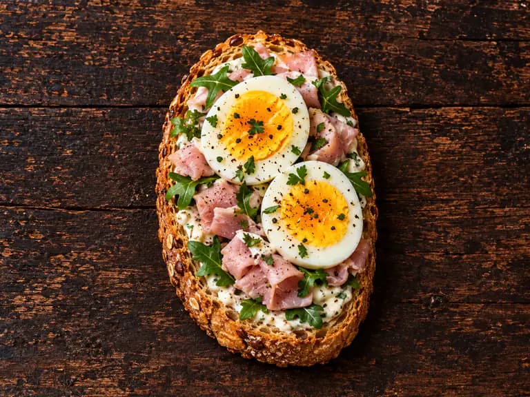 Bruschette con prosciutto cotto e uova con la farcitura su pane casereccio tostato, fotografate su un piano di legno scuro