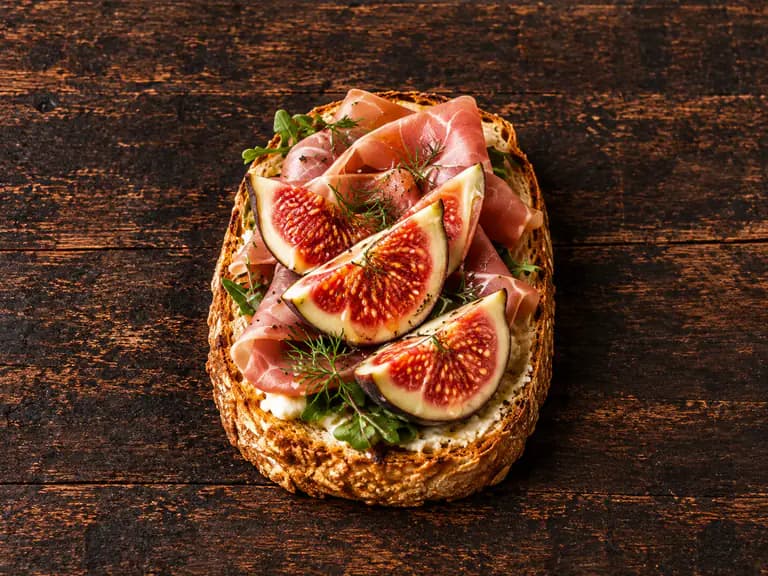Bruschette con prosciutto crudo e fichi con la farcitura su pane casereccio tostato, fotografate su un piano di legno scuro