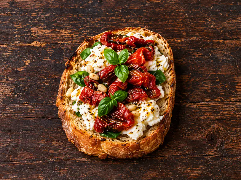 Bruschette con ricotta e pomodori secchi con la farcitura su pane casereccio tostato, fotografate su un piano di legno scuro