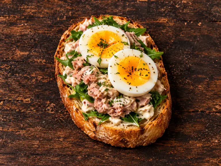 Bruschette con tonno e uova con la farcitura su pane casereccio tostato, fotografate su un piano di legno scuro