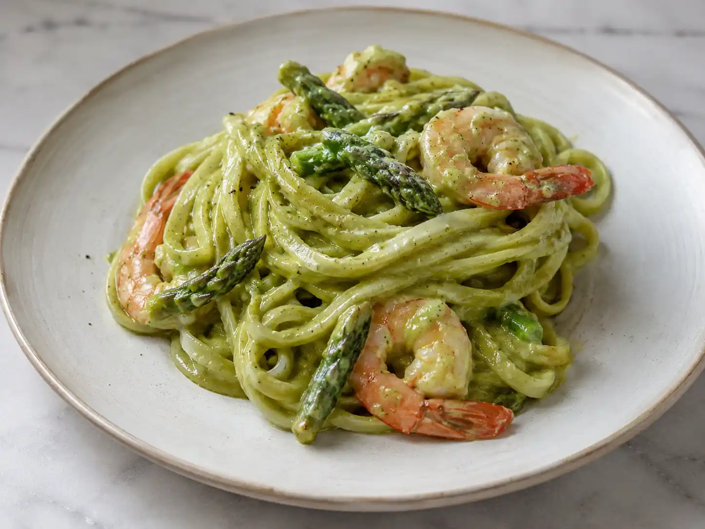 Pasta gamberi e asparagi cremosa con linguine, punte verdi e code di gambero in piatto chiaro