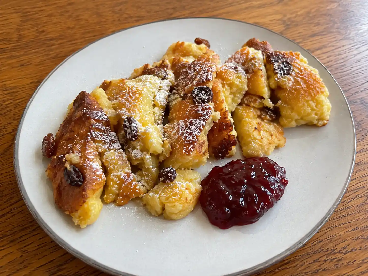 Kaiserschmarren ricetta tradizionale con pezzi soffici dorati, uvetta, zucchero a velo e confettura di mirtilli rossi