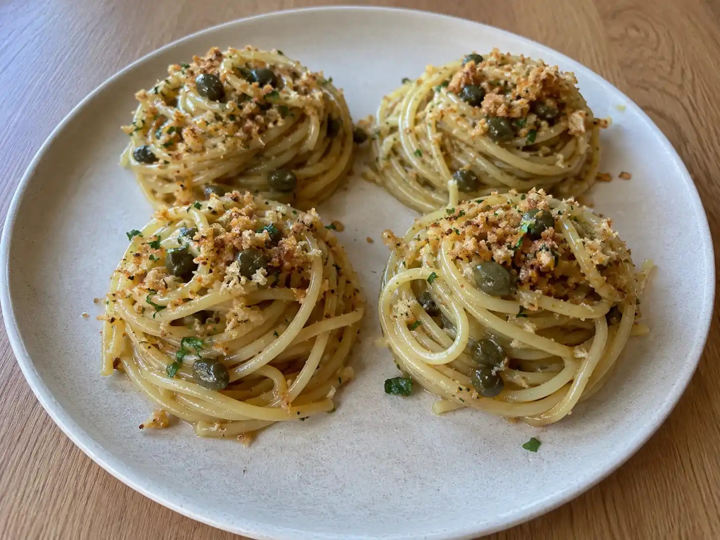 Pasta acciughe e capperi con spaghetti lucidi, capperi dissalati e mollica dorata in piatto chiaro