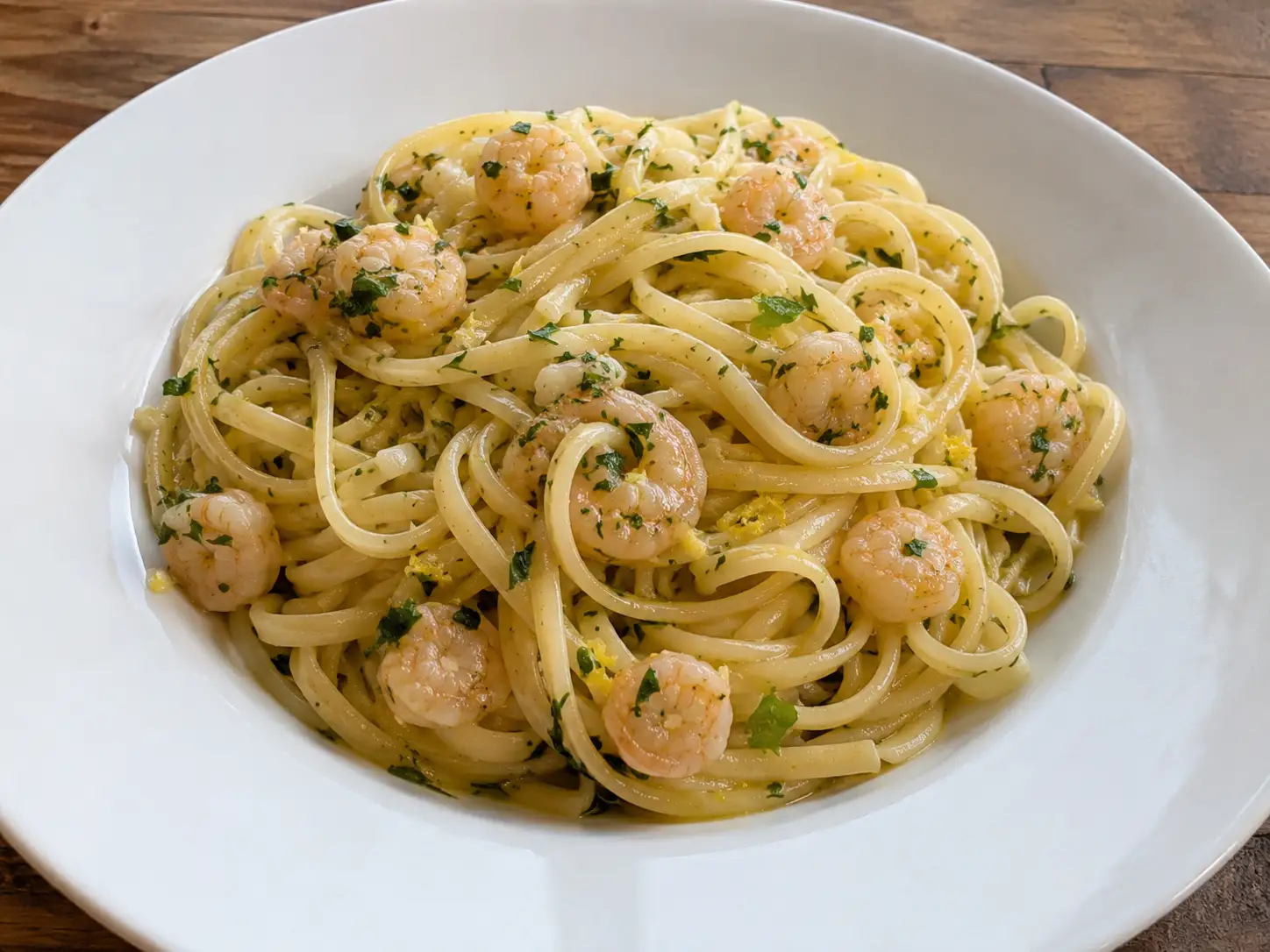 Pasta ai gamberetti in bianco con linguine lucide, prezzemolo e scorza di limone nel piatto