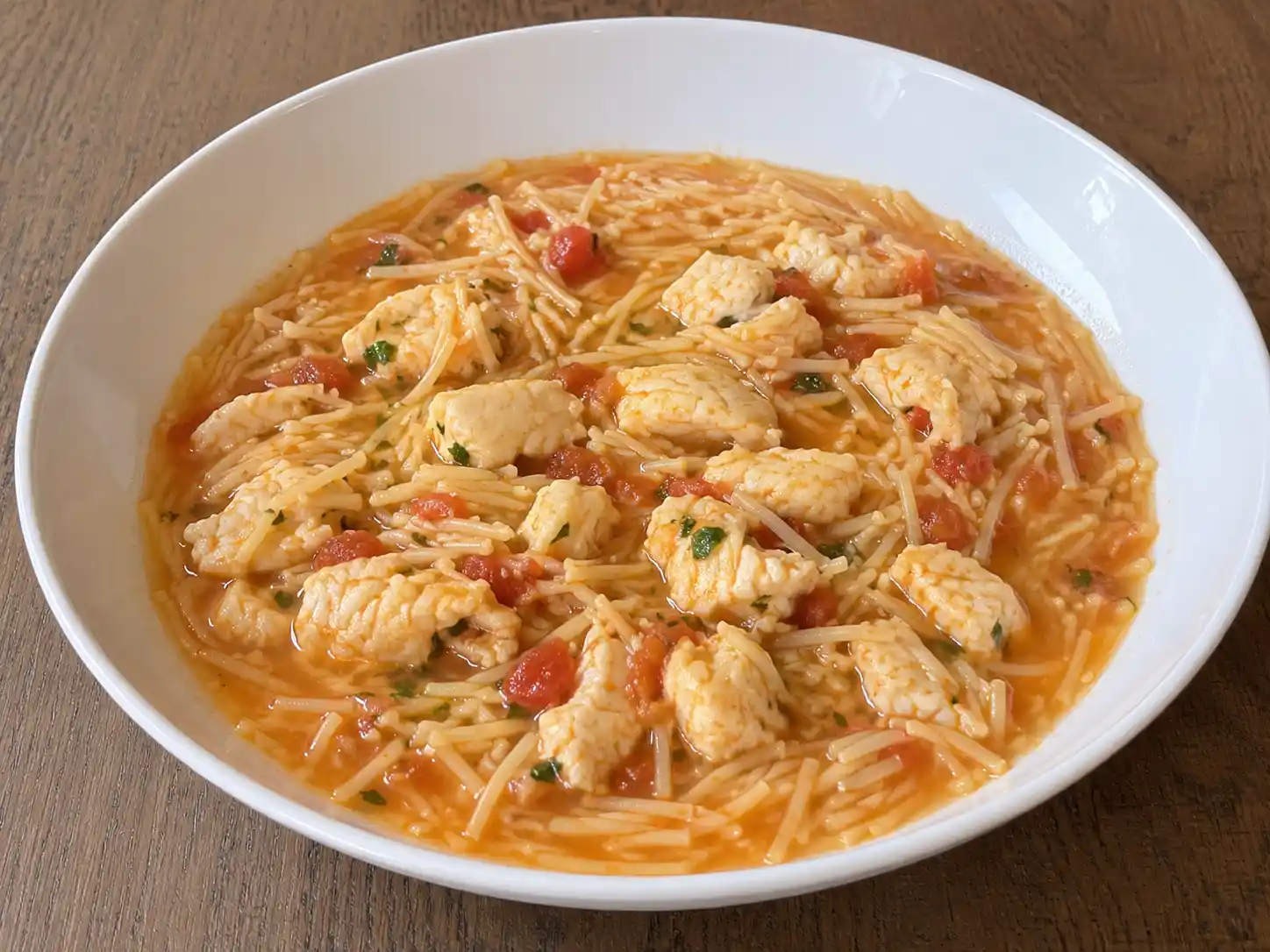 Pasta al brodo di pesce in ciotola con spaghetti spezzati, brodo rosato e pezzetti di pesce
