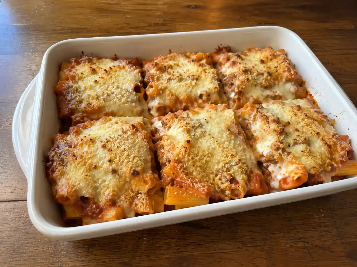 Pasta al forno al ragù in pirofila bianca con rigatoni, besciamella, mozzarella e crosta dorata