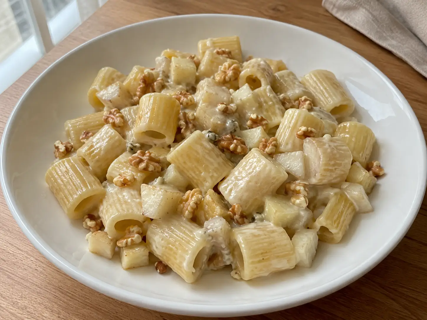 Pasta al gorgonzola e pere in piatto bianco con mezze maniche cremose, dadini di pera e noci