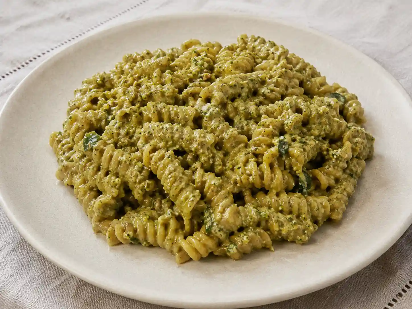 Pasta al pesto di pistacchio cremosa con granella, basilico e formaggio su piatto chiaro