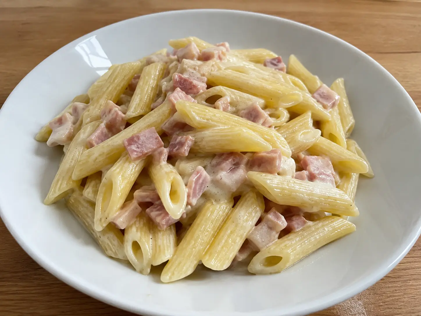 Pasta al prosciutto cotto cremosa con penne rigate, panna e dadini dorati in piatto bianco