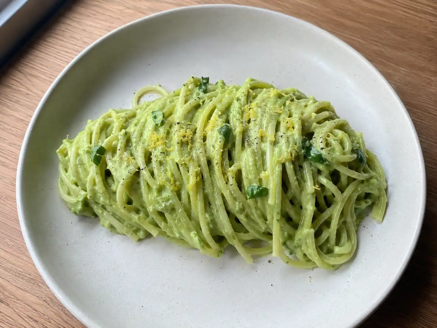 Pasta avocado cremosa con spaghetti, crema verde al limone e basilico servita in piatto chiaro