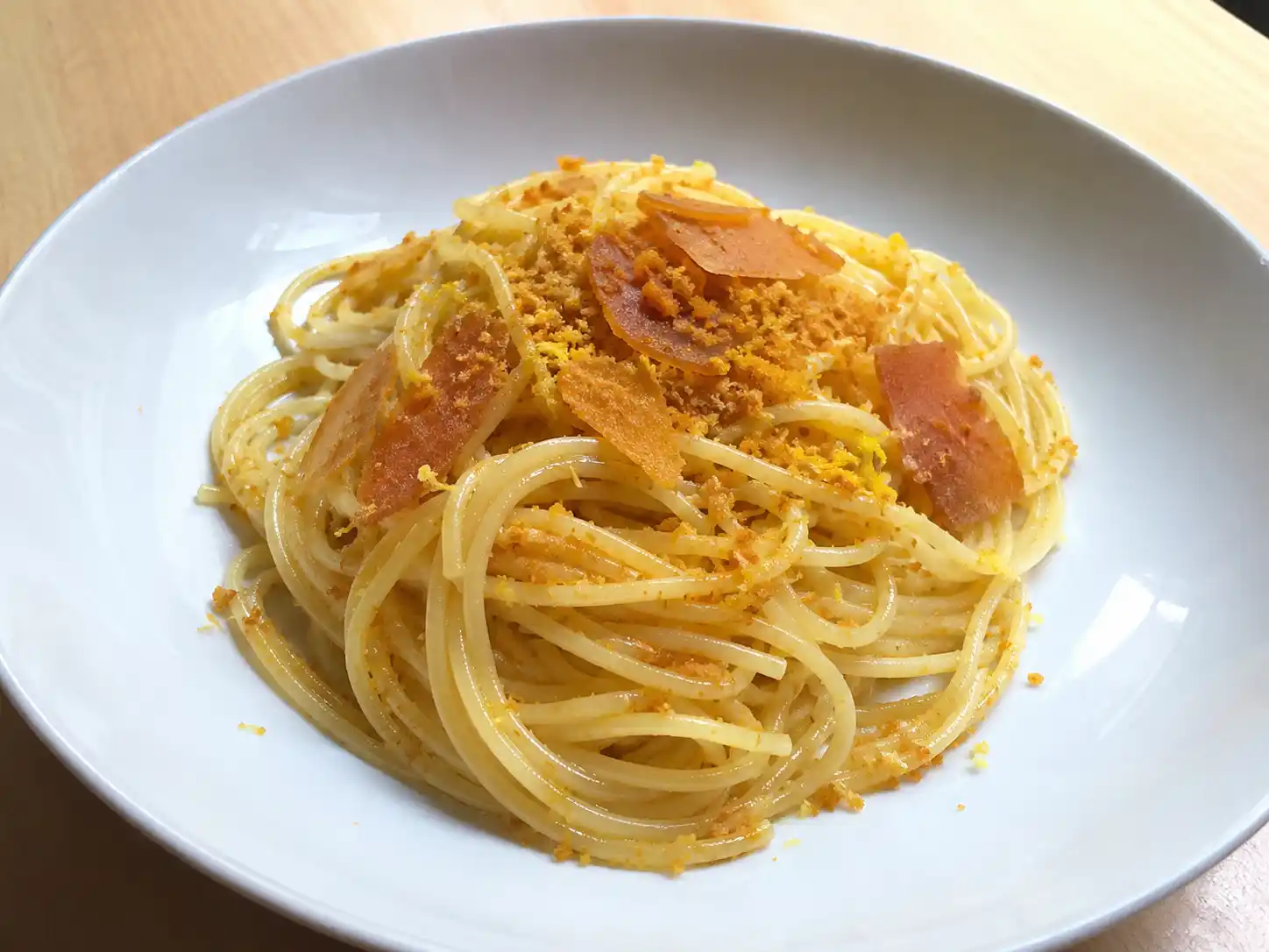 Pasta bottarga e limone in piatto fondo con spaghetti lucidi, bottarga grattugiata e scorza