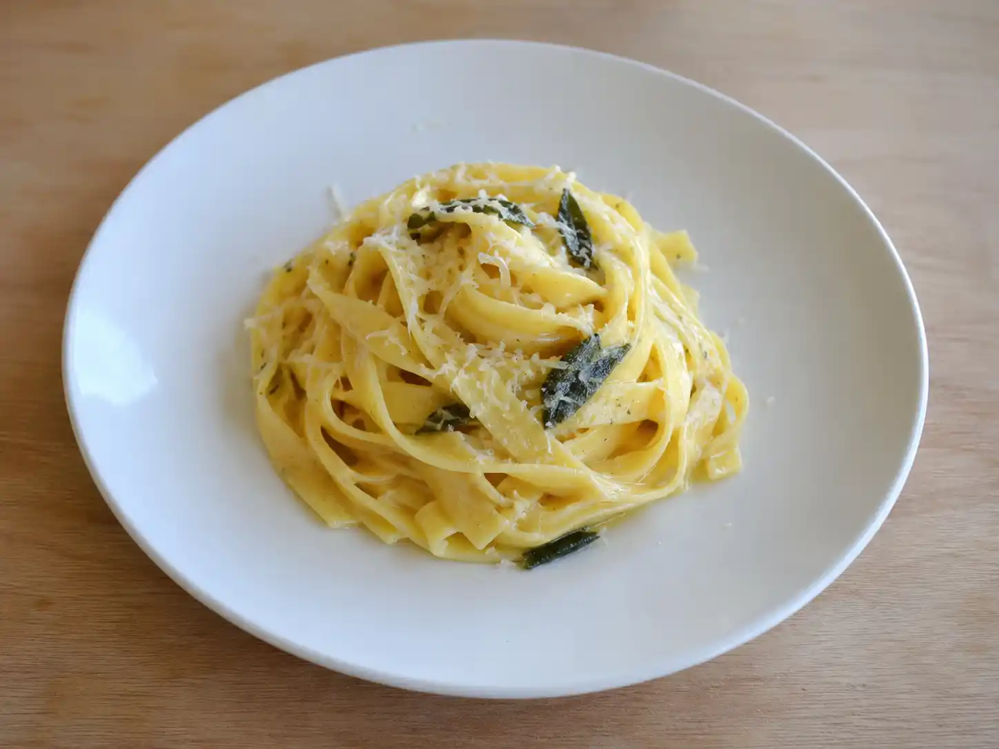 Pasta burro e salvia con tagliatelle lucide, foglie croccanti e parmigiano su piatto chiaro