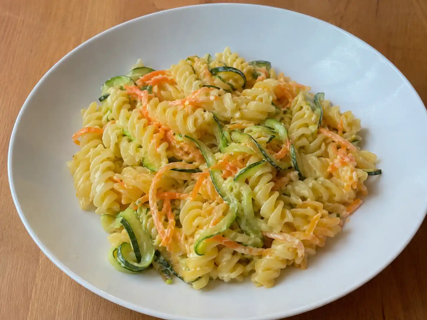 Pasta carote e zucchine cremosa con fusilli, verdure a listarelle e Parmigiano in piatto bianco