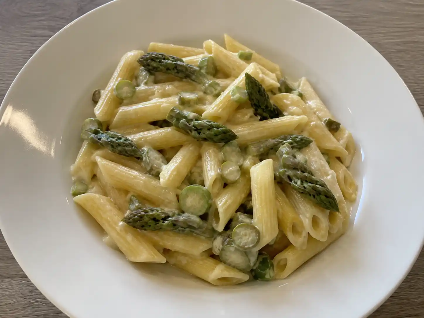 Pasta con asparagi e panna cremosa con penne rigate, punte verdi e salsa chiara in piatto fondo