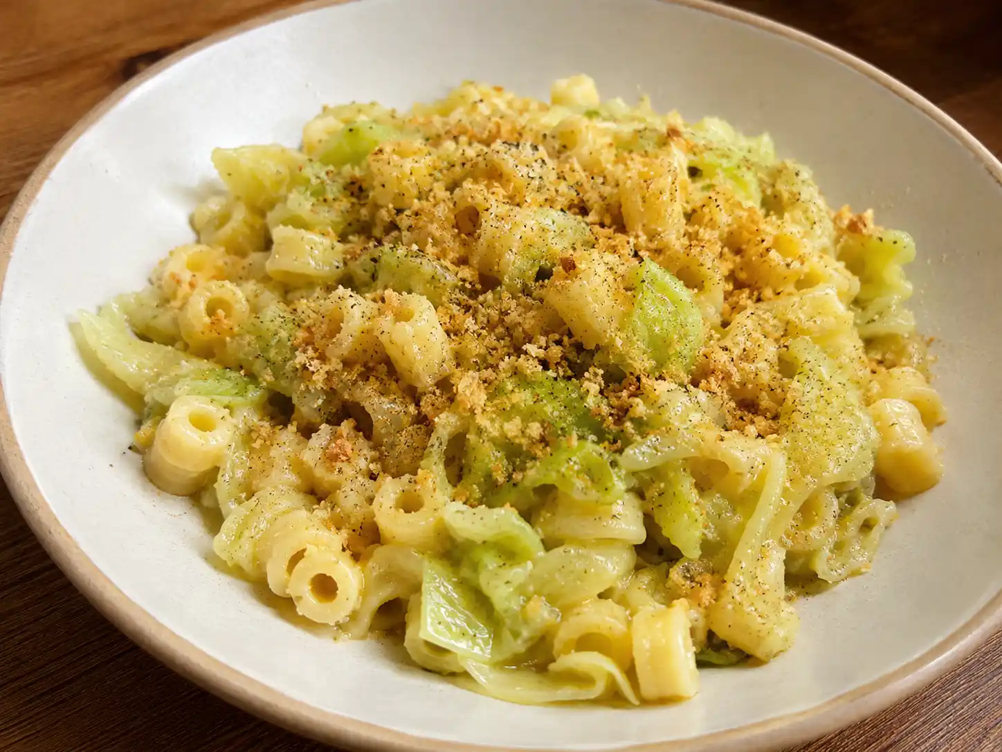 Pasta con cavolo cappuccio cremosa con pangrattato tostato in piatto fondo chiaro