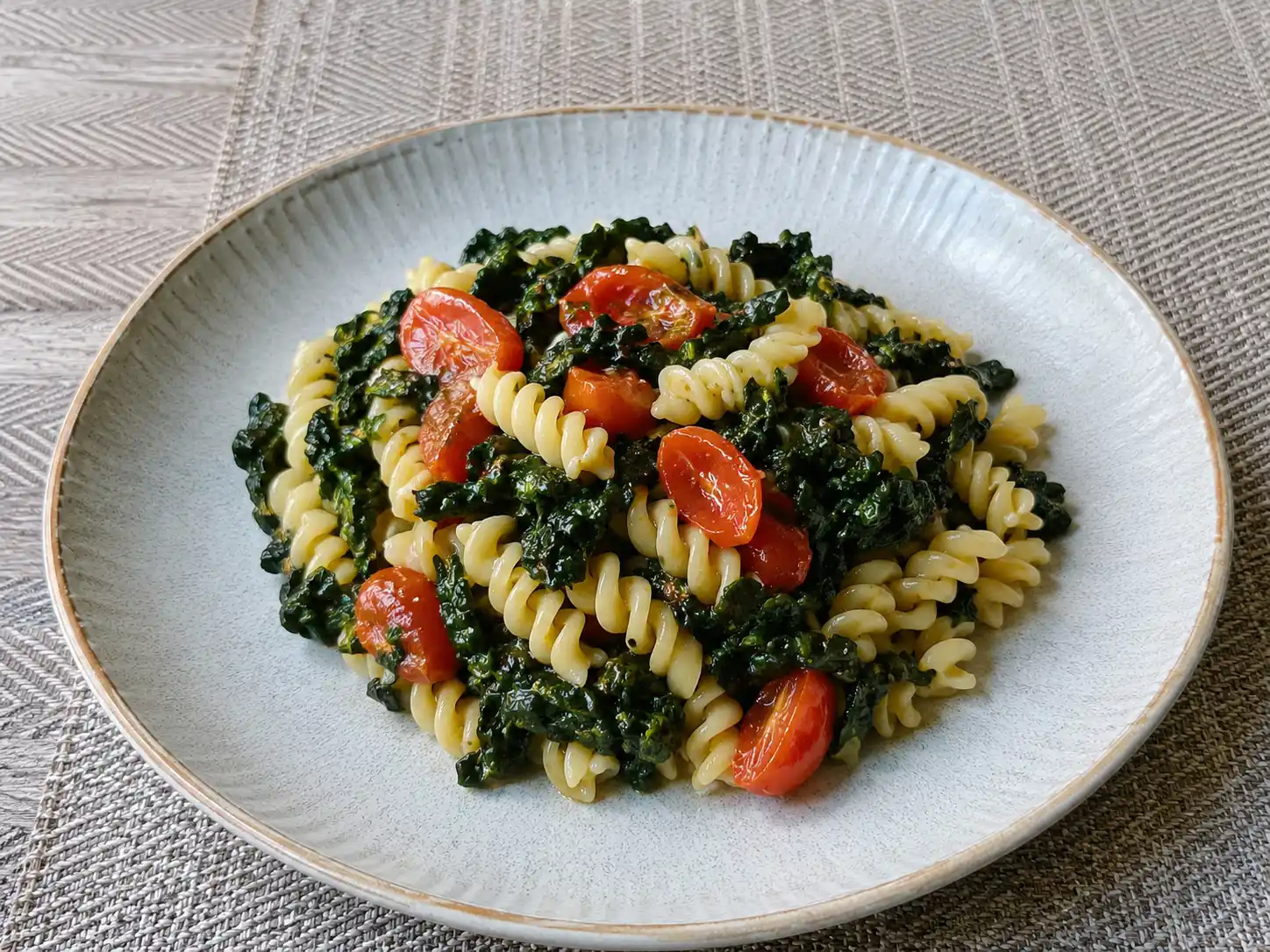 Pasta con cavolo nero e pomodorini in piatto fondo, con fusilli verdi e datterini appassiti