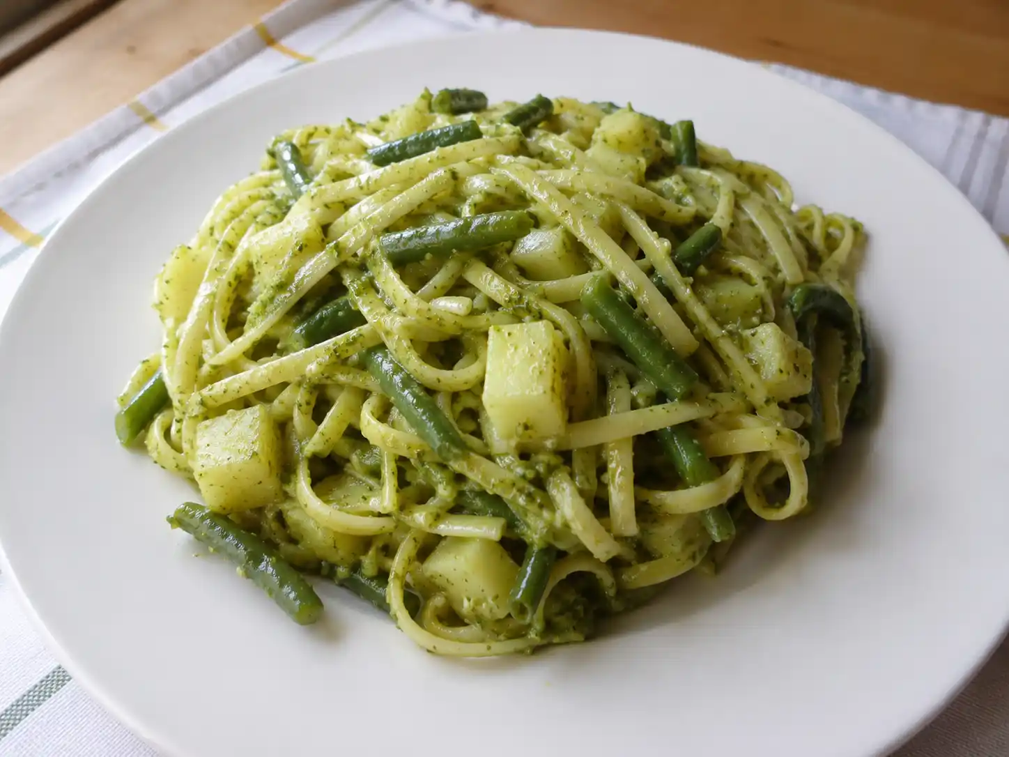 Pasta con fagiolini e patate al pesto in piatto bianco, con trenette cremose e verdure a pezzetti