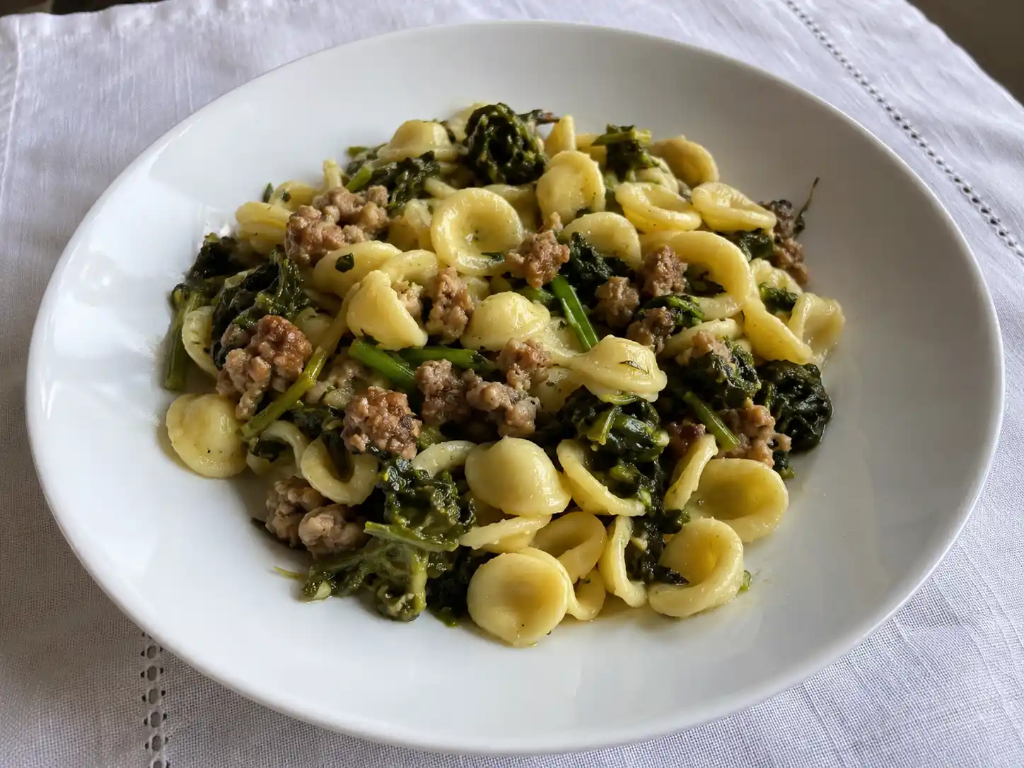 Pasta con friarielli e salsiccia in piatto piano, orecchiette lucide con verdure verdi e carne