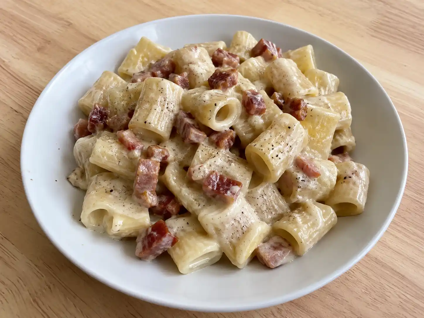 Pasta con gorgonzola e pancetta in piatto bianco, con mezze maniche cremose e cubetti dorati