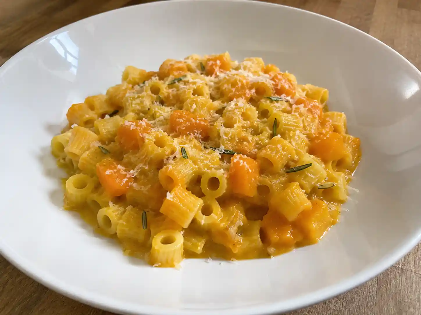 Pasta con la zucca cremosa in piatto fondo bianco con ditalini avvolti da crema di zucca dorata