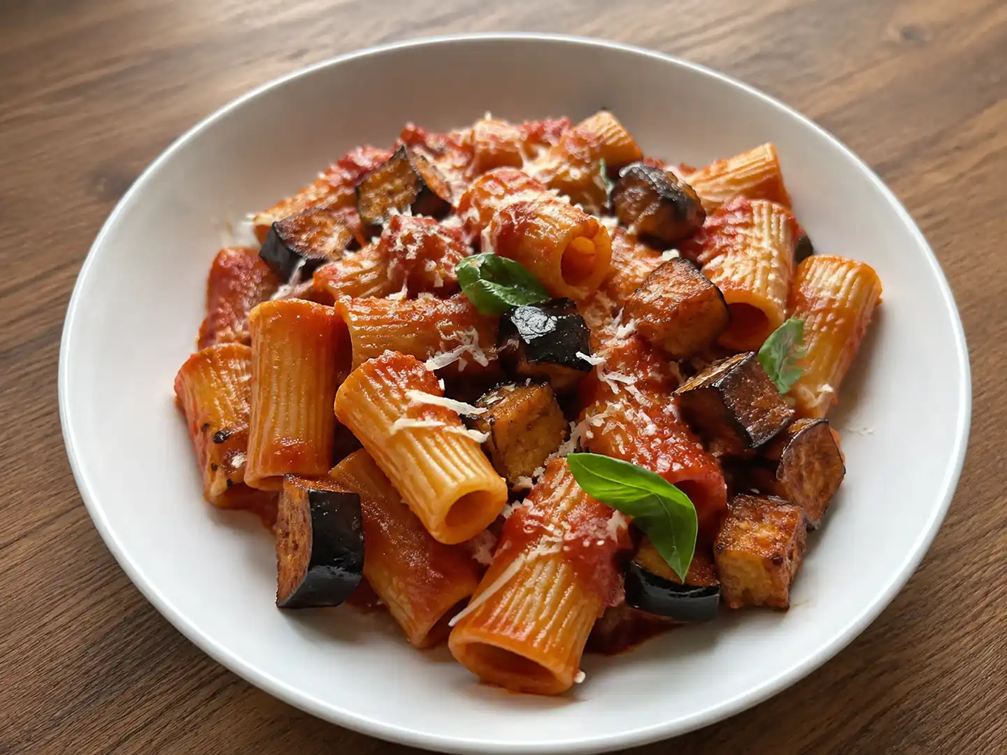 Pasta con le melanzane fritte al pomodoro con ricotta salata e basilico in piatto fondo
