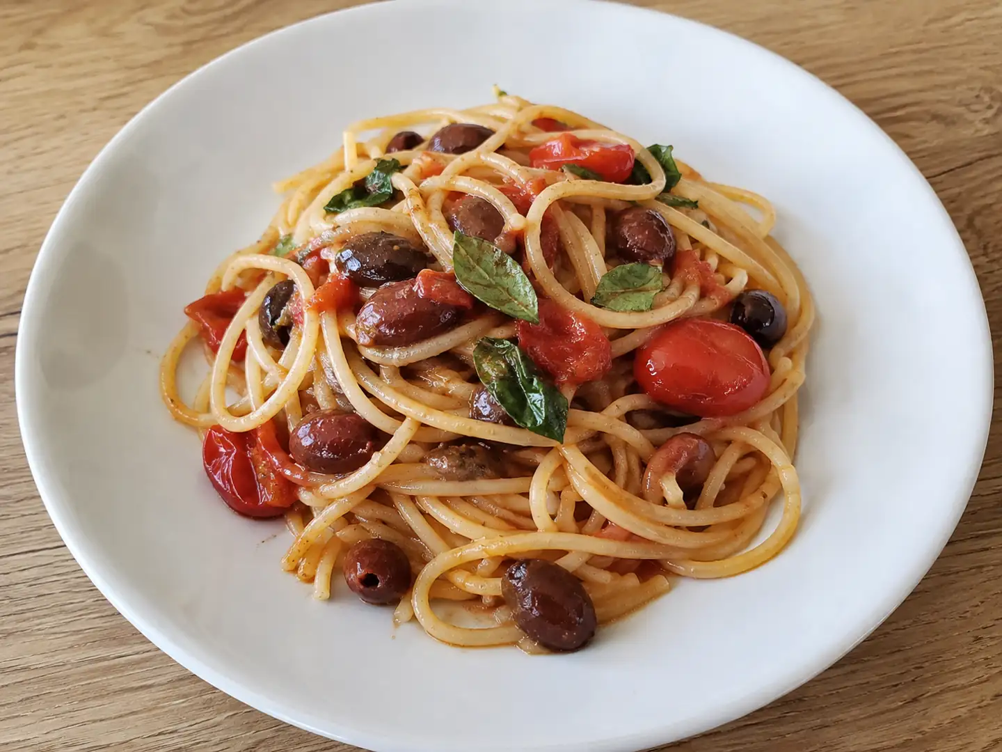 Pasta con olive taggiasche e pomodorini saltata in padella, servita con basilico fresco