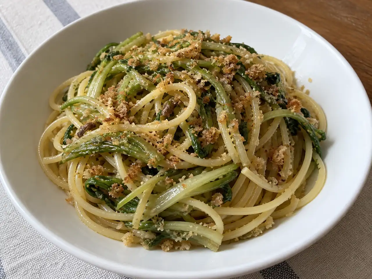 Pasta con puntarelle e alici con pangrattato tostato, servita calda in un piatto fondo bianco