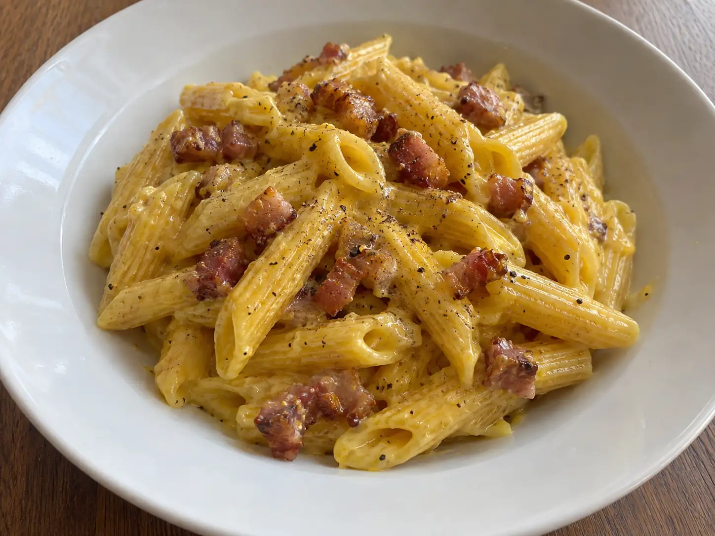 Pasta con zafferano e pancetta cremosa in piatto fondo, dorata e con cubetti rosolati