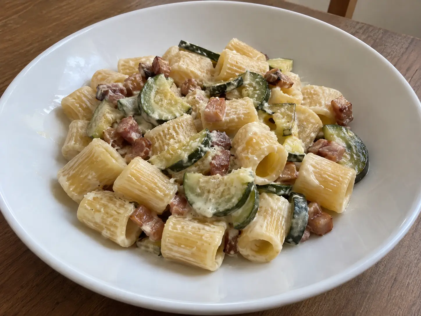 Pasta con zucchine pancetta e panna in piatto bianco, cremosa e con cubetti dorati visibili