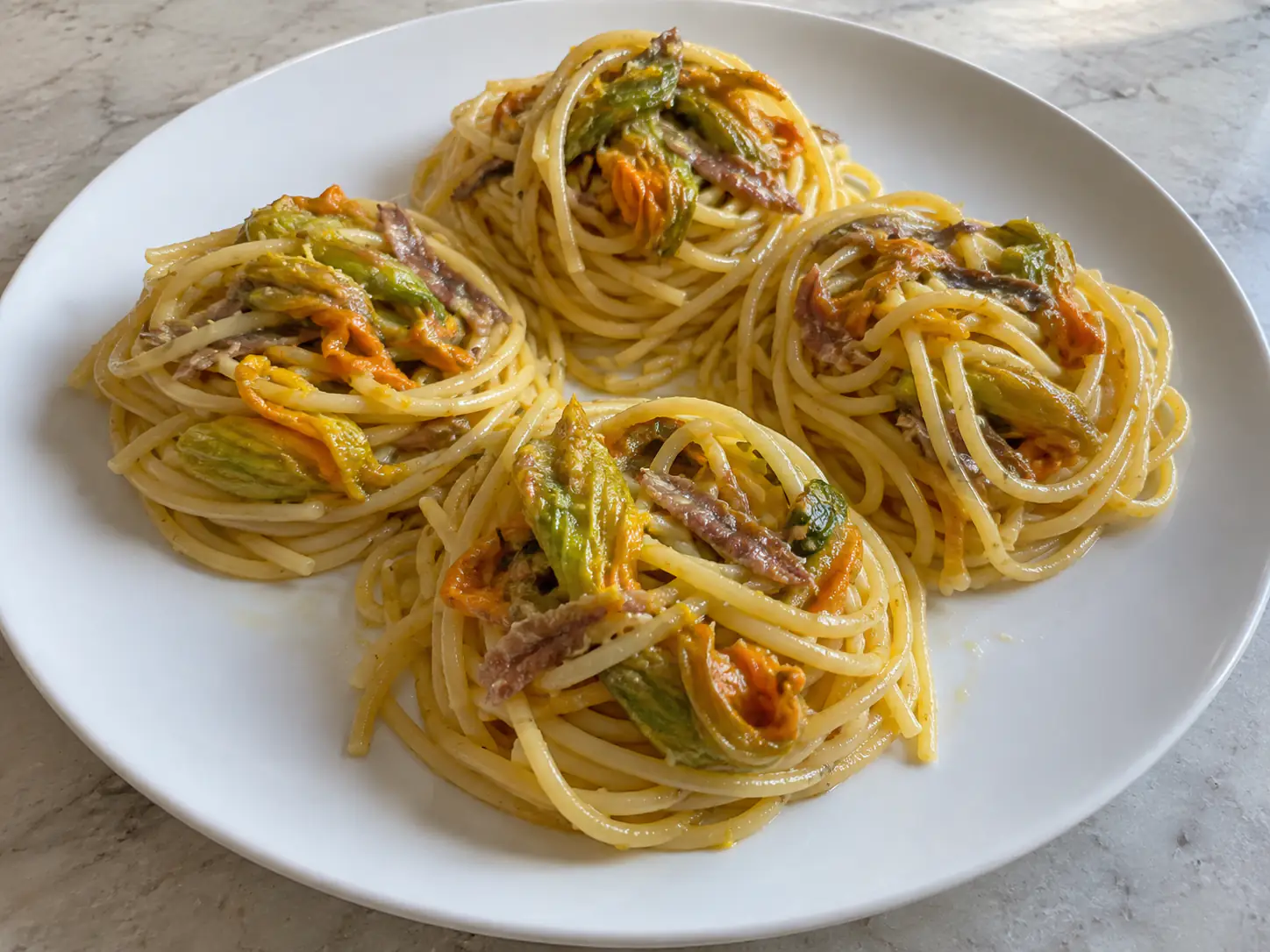 Pasta fiori di zucca e alici con spaghetti, alici sciolte, fiori teneri e scorza di limone