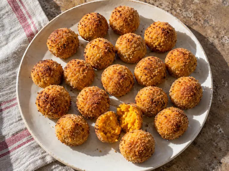 Polpette di zucca piccole e dorate su un piatto chiaro, con panatura sottile e interno arancione morbido