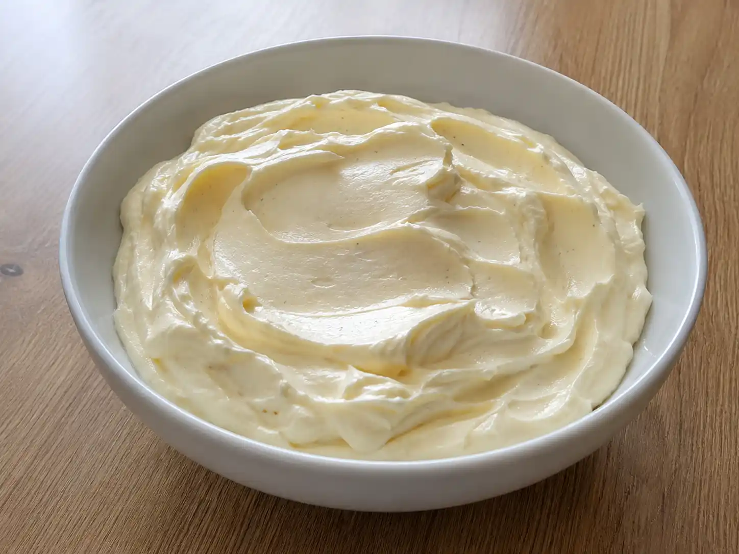 Crema mascarpone e panna per tiramisù in ciotola bianca, soda e liscia con venature di vaniglia