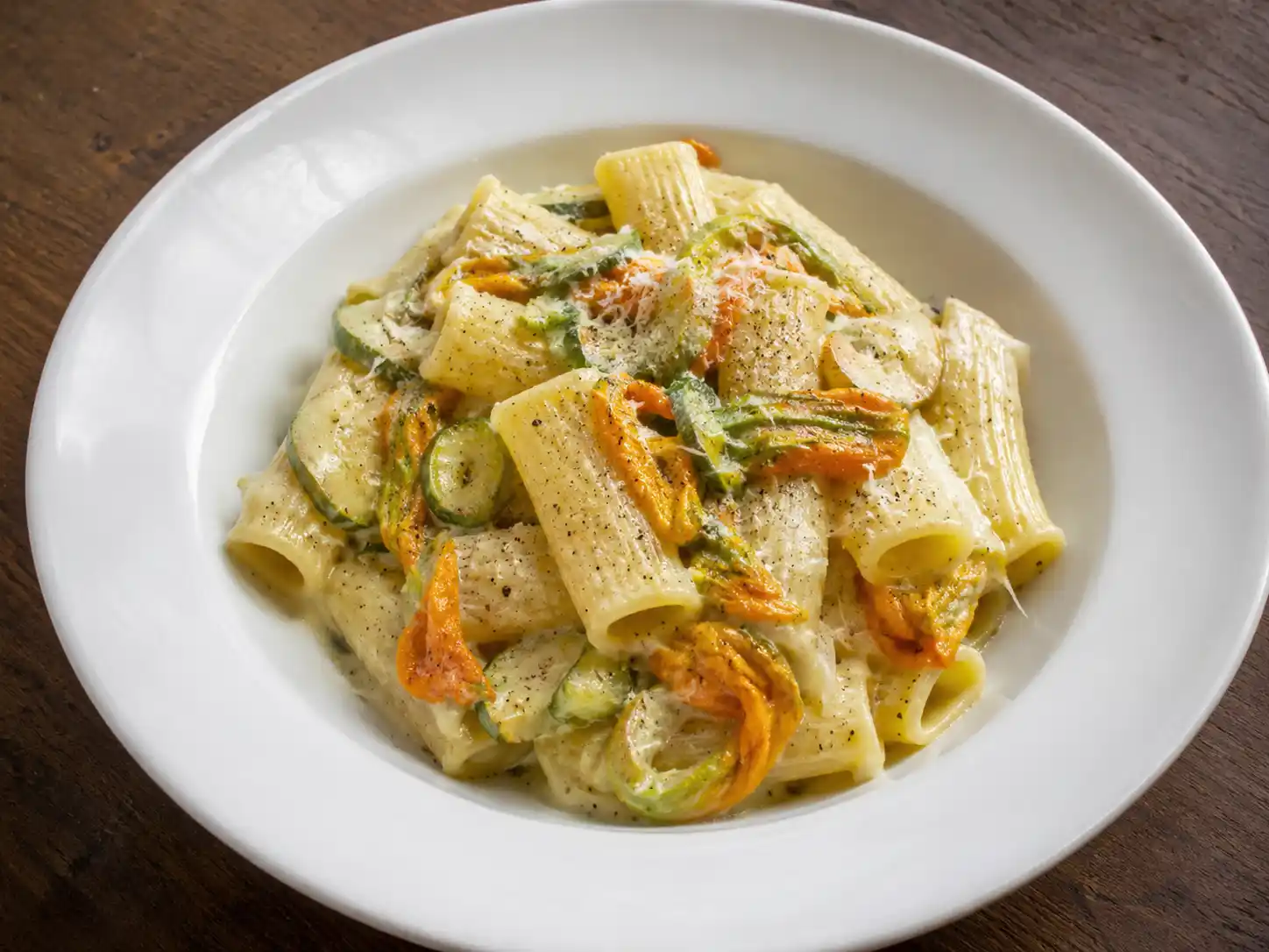 Pasta con fiori di zucca cremosa con zucchine, acciughe e pecorino in piatto fondo bianco
