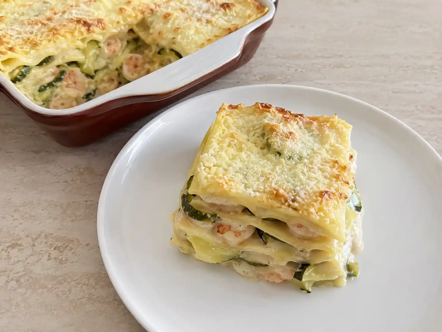 Lasagne con gamberetti e zucchine cremose, servite in teglia con strati chiari e superficie dorata