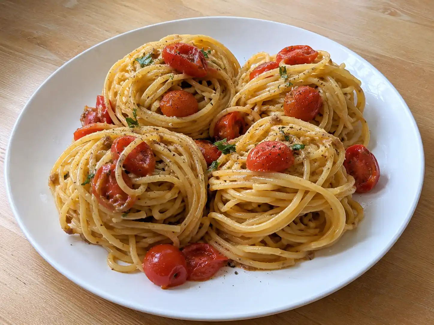 Pasta acciughe e pomodorini in piatto bianco con spaghetti, pomodorini cotti e prezzemolo fresco