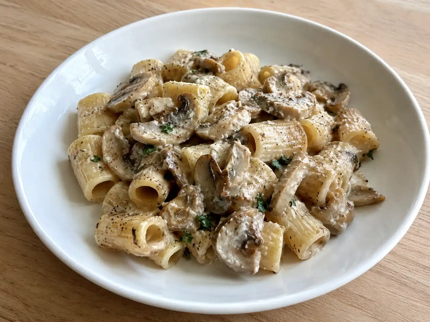 Pasta ai funghi cardoncelli cremosa senza panna con prezzemolo e funghi dorati in piatto chiaro