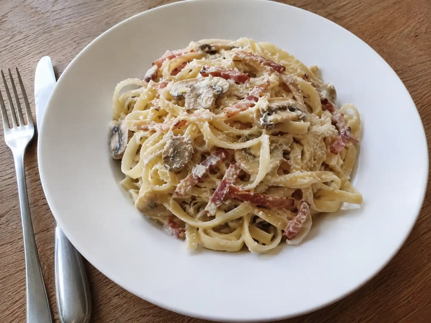 Pasta alla tirolese cremosa con speck, funghi champignon e tagliatelle in piatto fondo