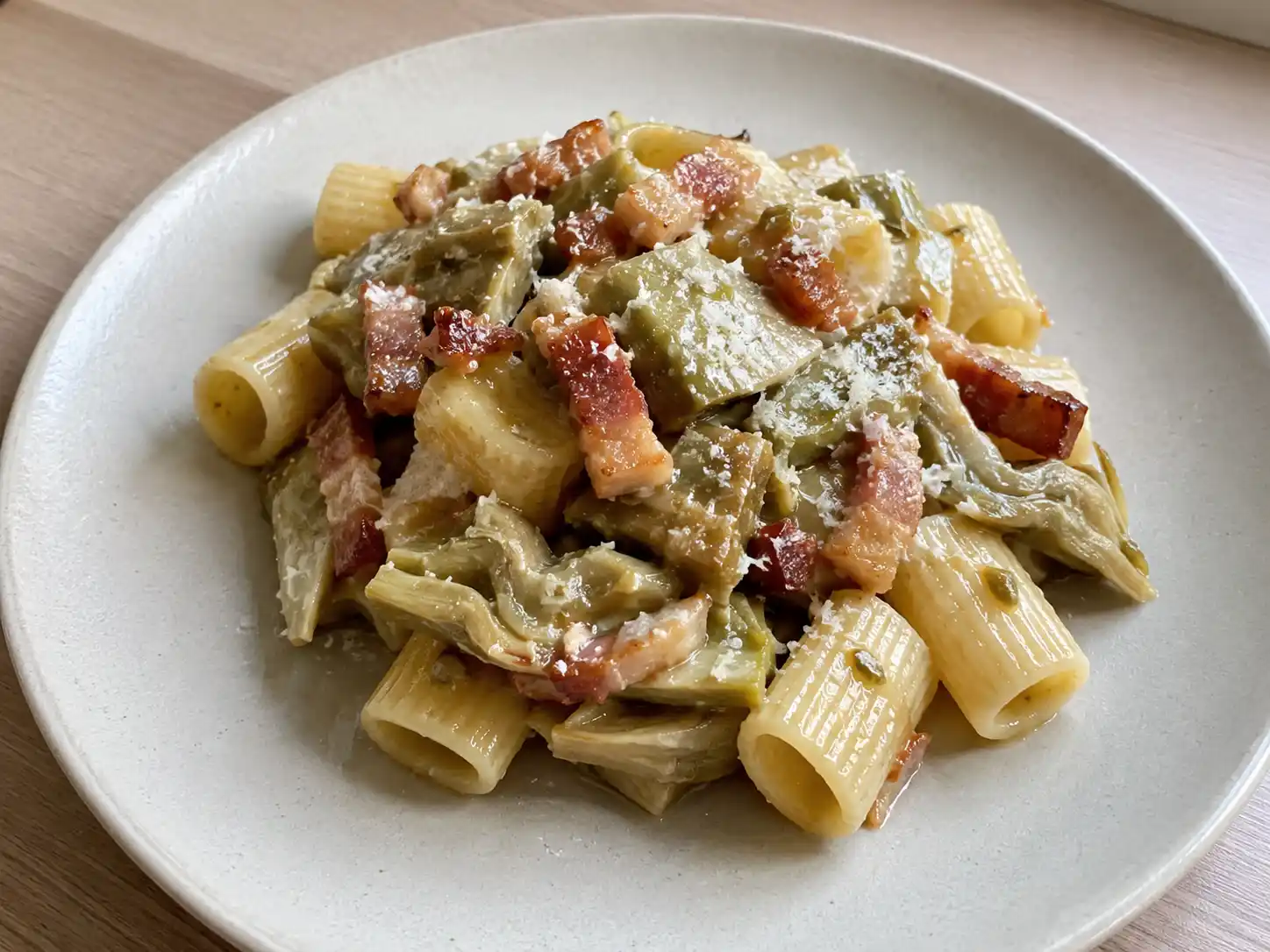 Pasta carciofi e guanciale in piatto chiaro con guanciale croccante e carciofi teneri