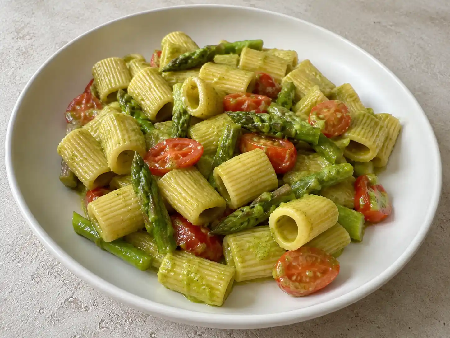 Pasta con asparagi e pomodorini in piatto bianco, cremosa con punte verdi e datterini morbidi