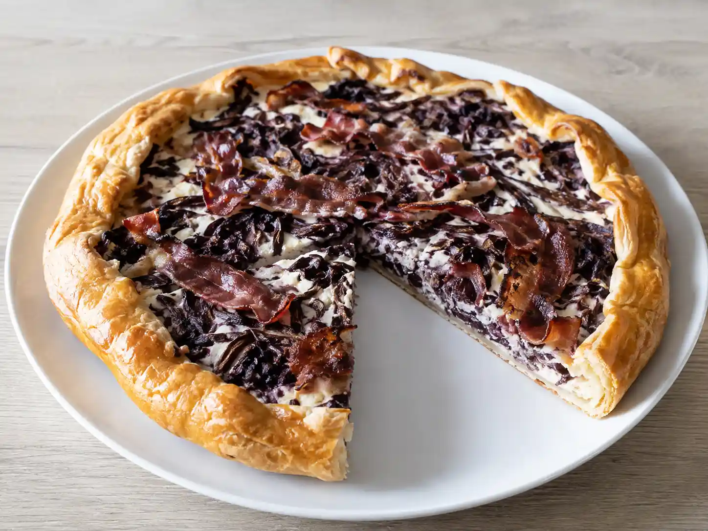 Torta salata radicchio e speck a fette, con pasta sfoglia dorata e ripieno viola cremoso